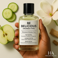 A bottle of Be Delicious (Women Type) Body Oil held by a dark-skinned hand, surrounded by green apples, cucumber slices, magnolia petals, and soft amber, with the HA Fragrances logo in the corner.