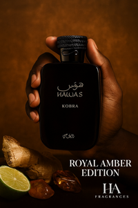 Dark-skinned hand holding Rasasi Hawas Kobra Eau De Parfum bottle – Royal Amber Edition, surrounded by ginger root, lime, and amber stones on a warm golden background with HA Fragrances branding.