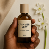 Cashmere Mist Women Type fragrance oil bottle held by a dark-skinned hand with white lily flowers and beige fabric in the background – soft, powdery, floral perfume oil for women.